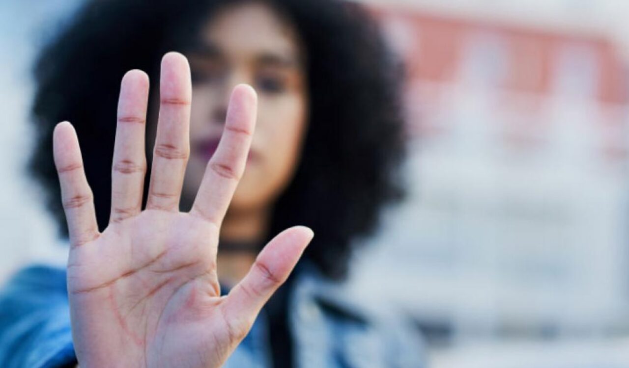 Junge Frau die ihre Hand in abwehrender Haltung vors gesicht hält.