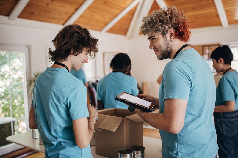 Eine gemischte Gruppe von männlichen und weiblichen Freiwilligen sortiert gemeinsam Spenden in Kartons in einem Wohltätigkeitszentrum.