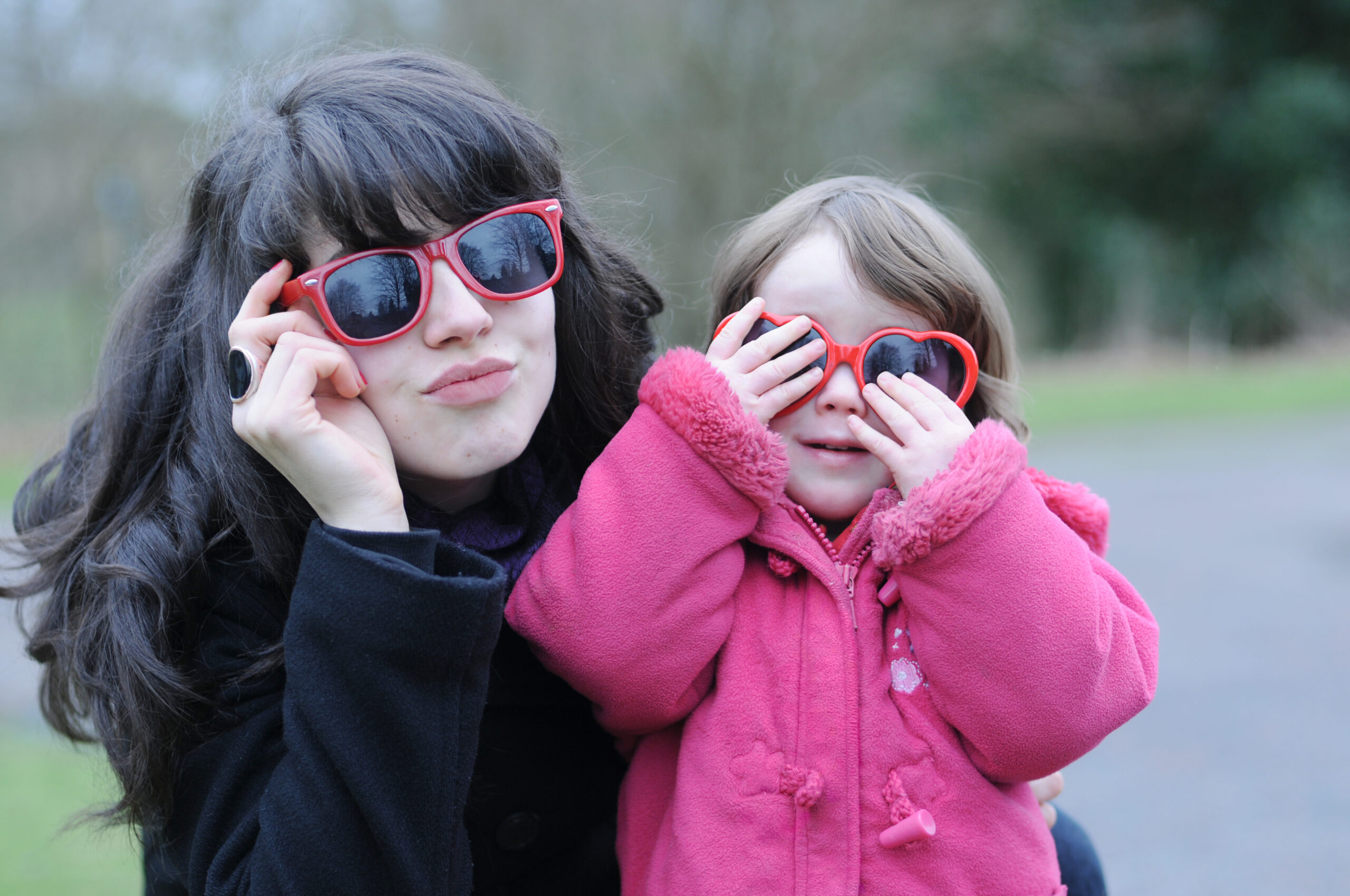 Junge Frau, Au-pair mit kleinem Mädchen. Beide tragen eine rote Sonnenbrille