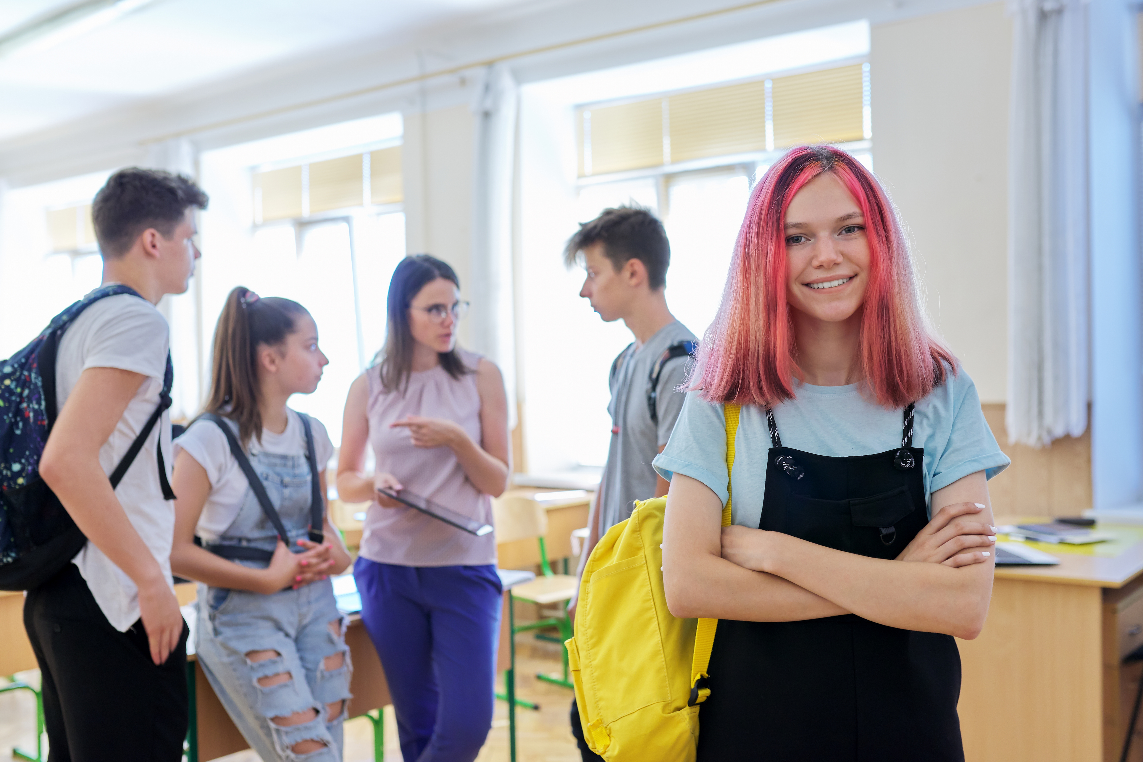 Schülerin, die in die Kamera blickt, im Klassenzimmer mit einer Gruppe von Schülerinnen und Schülern.