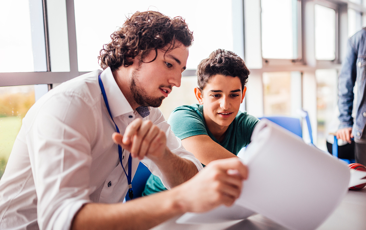 Junger Mann lernt mit einem Schüler, sie schauen gemeinsam auf Unterlagen.