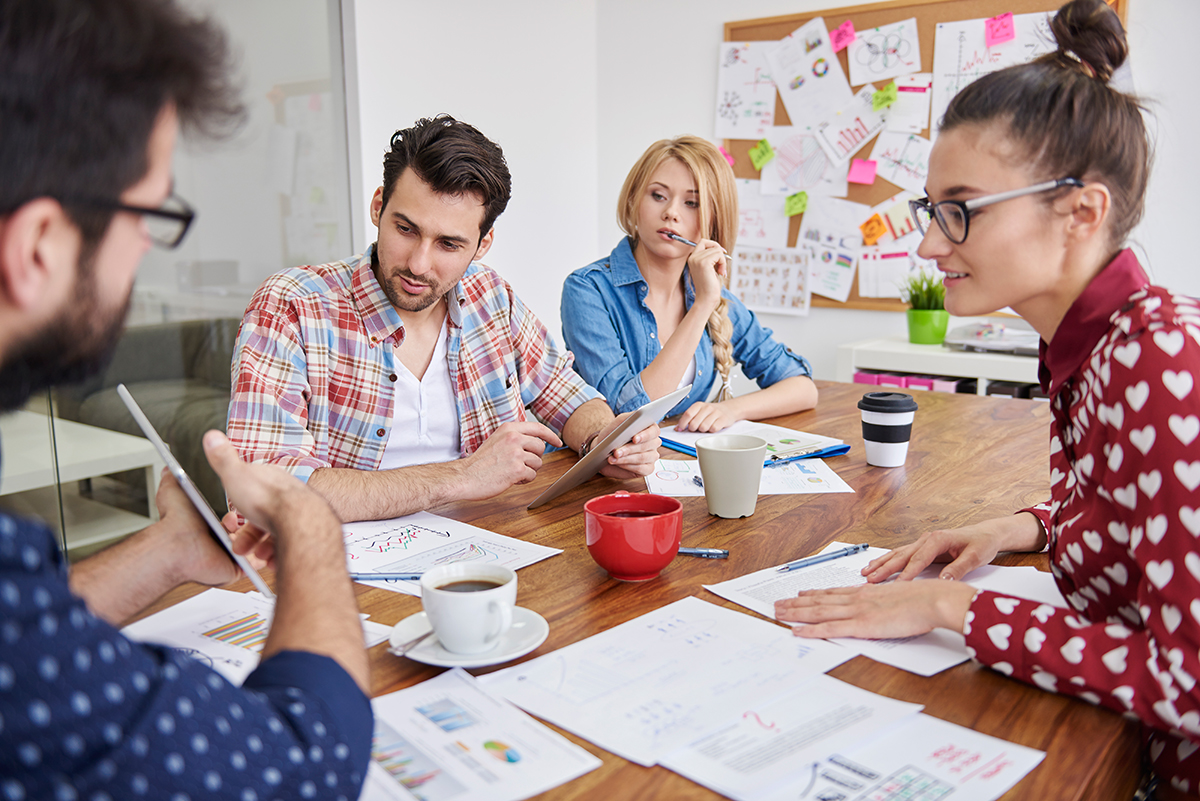 Ein junges Team sitzt zusammen um einen Besprechungstisch mit vielen Unterlagen darauf.