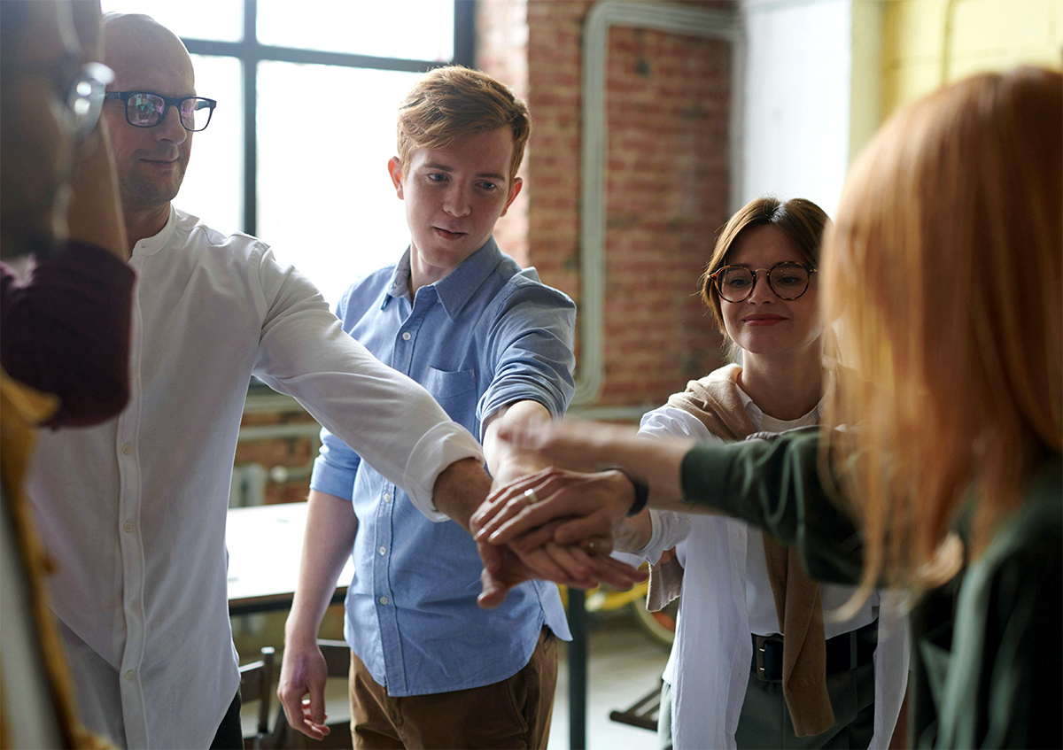 Junge Menschen bilden einen Kreis und legen ihre Hände in die Mitte um so gemeinsam einzuschlagen.