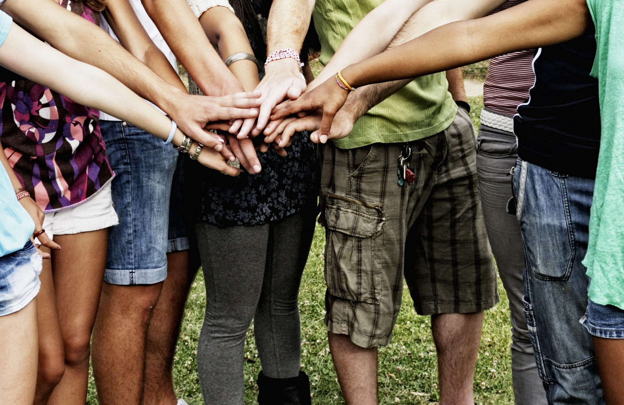 Jugendliche stehen im Kreis und halten die Hände übereinander. Man sieht nur Hände und Beine.