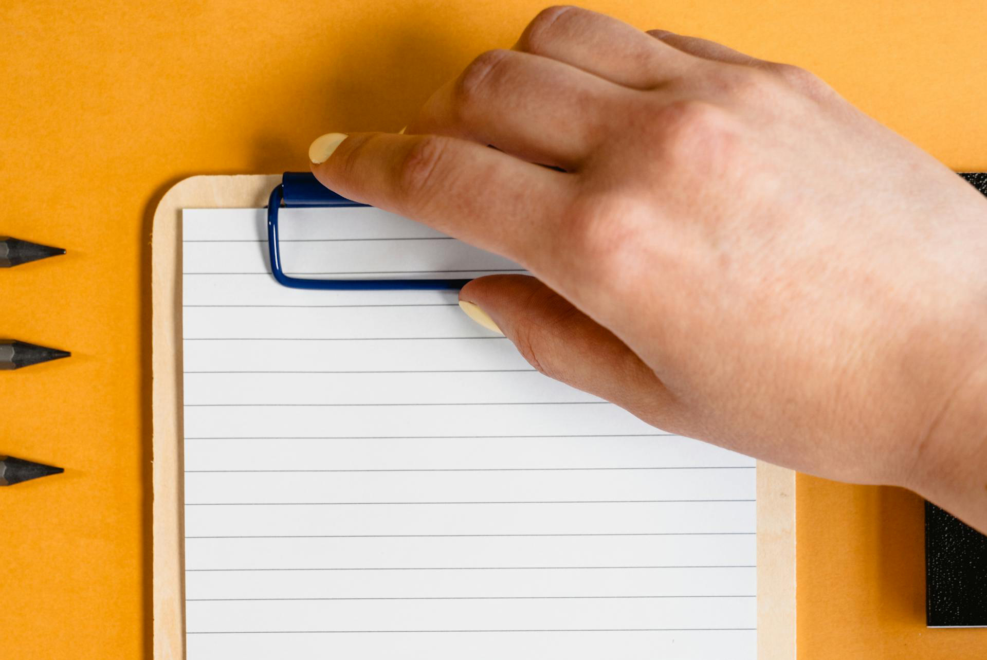 Hand die ein Clipboard hält vor gelbem Hintergrund.