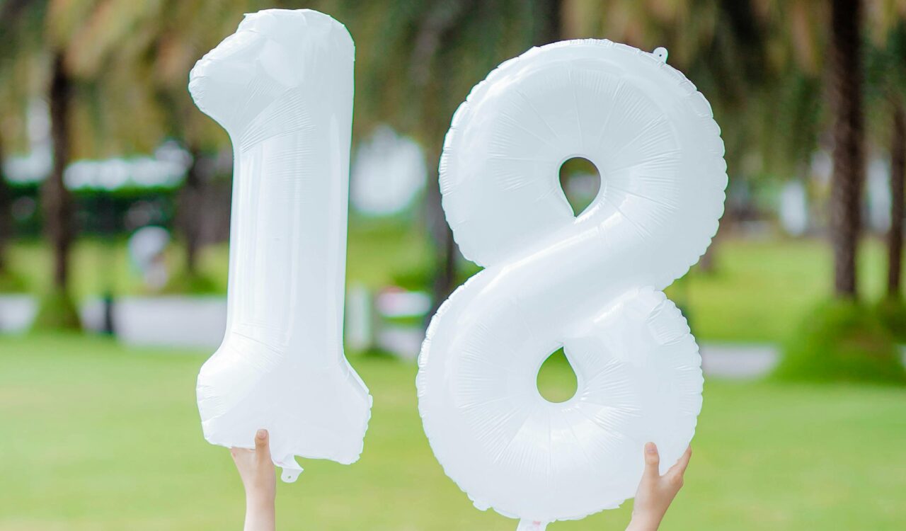 Ein Mädchen feiert ihren 18. Geburtstag und hält Luftballons in Form der Ziffern 18 hoch.