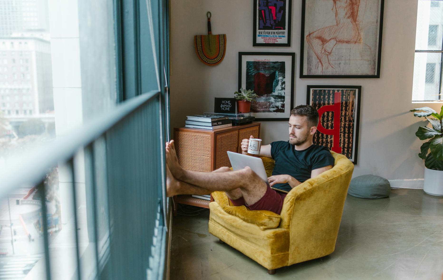 Junger Mann sitzt mit seinem Laptop auf einem Fauteuil in seiner Wohnung.
