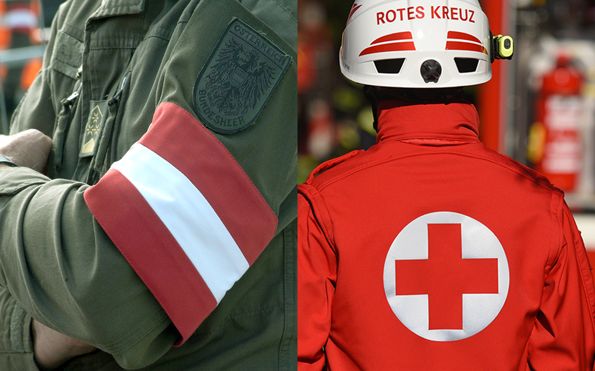 Nahaufnahme eines Soldaten, man sieht nur den Oberkörper, im Vordergrund seinen Arm mit Österreich-Fahne und Aufnäher "Österreichisches Bundesheer". Rechts den Rücken eines Rot-Kreuz-Mitarbeiters mit Helm.